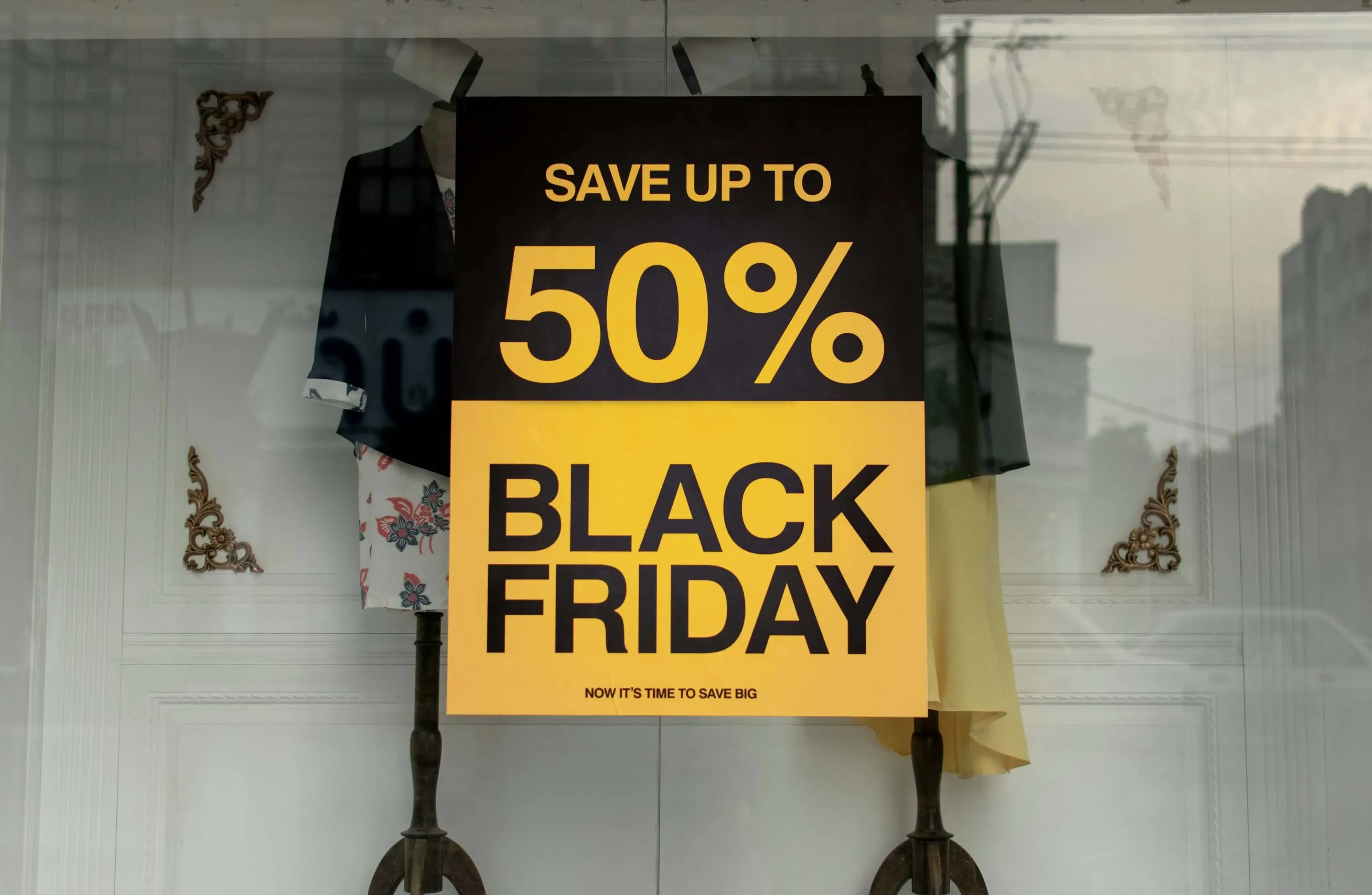 Black and yellow sign in a store window advertising Black Friday sale with savings up to 50%.